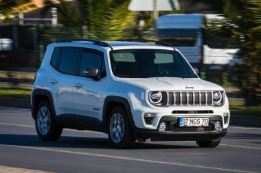 Alanya, Türkiye 19 Nisan 2021: Beyaz Jeep Renegade sıcak bir yaz gününde palmiyelerin arkasına doğru hızla sürüyor 