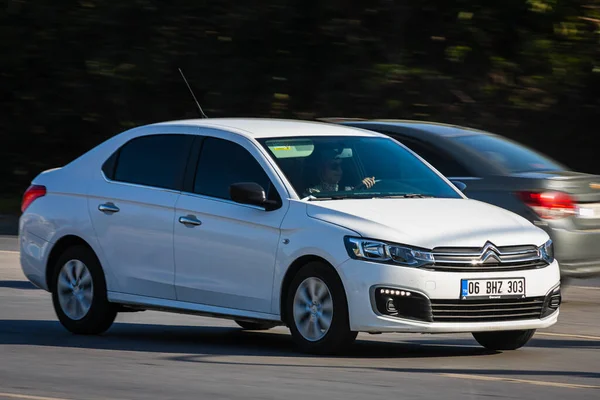 Alanya, Türkiye 17 Nisan 2021: Beyaz Citroen C-Elysee sıcak bir yaz gününde palmiyelerin arka planına doğru hızla sürüyor  