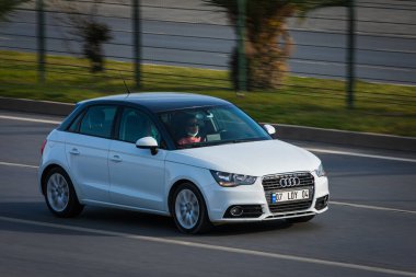 Alanya, Türkiye 17 Nisan 2021: Beyaz Audi A1 sıcak bir yaz gününde palmiyelerin arkasına doğru hızla sürüyor  