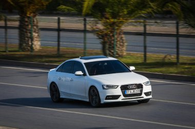 Alanya, Türkiye 17 Nisan 2021: Beyaz Audi A4 sıcak bir yaz gününde palmiyelerin arkasına doğru hızla sürüyor  