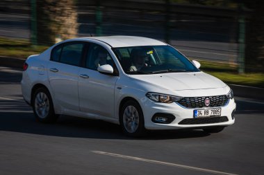 Alanya, Türkiye 17 Nisan 2021: Beyaz Fiat Albea sıcak bir yaz gününde palmiyelerin arkasına doğru hızla sürüyor  