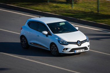 Alanya, Türkiye 19 Nisan 2021: Beyaz Renault Clio sıcak bir yaz gününde palmiyelerin arkasına doğru hızla sürüyor  