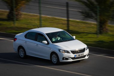 Alanya, Türkiye 17 Nisan 2021: Beyaz Peugeot 301 sıcak bir yaz gününde bir palmiye ağacının arka planına doğru hızla sürüyor  