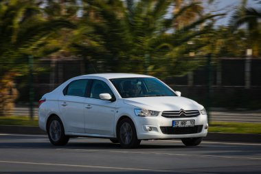 Alanya, Türkiye 17 Nisan 2021: Beyaz Citroen C-Elysee sıcak bir yaz gününde palmiyelerin arka planına doğru hızla sürüyor  