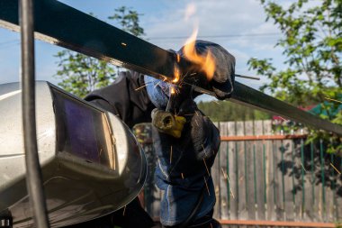 Kaynak makinesinin kapağı köydeki inşaat sahasında bir tel örgü örüyor. Metal bir çerçeve üzerinde inşaat.