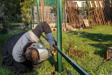 Kaynak makinesinin kapağı köydeki inşaat sahasında bir tel örgü örüyor. Metal bir çerçeve üzerinde inşaat.