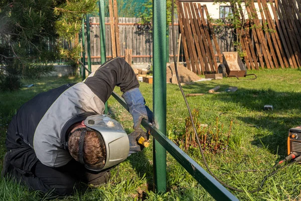 Kaynak makinesinin kapağı köydeki inşaat sahasında bir tel örgü örüyor. Metal bir çerçeve üzerinde inşaat.