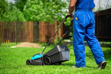 A man with an electric lawn mower mowing the lawn.Adult man pruning and landscaping a garden, mowing grass, lawn, paths. clipart