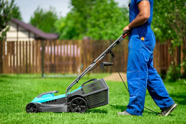 Lawn grass mowing. Worker cutting grass in a green yard. A man with an electric lawn mower mowing a lawn. Gardener pruning a garden