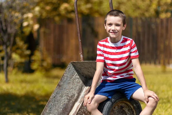 田舎の家の庭にあるガーデンホイールバローに座っている男の子 掘る準備ができている小さな男の子のヘルパー — ストック写真