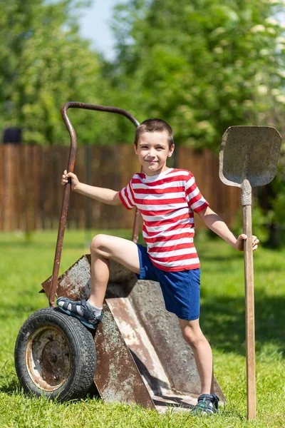 Ein Kleiner Fröhlicher Junge Steht Auf Einer Gartenschubkarre Und Hält — Stockfoto