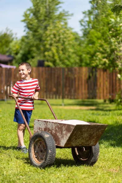 小さな男の子が庭の晴れた日に袋付きの車列を運転します 庭の少年補佐 — ストック写真