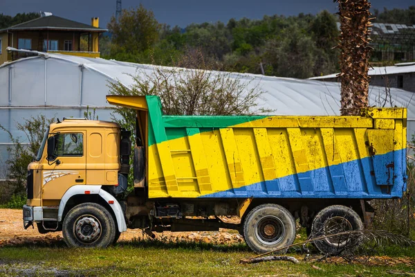 Dump truck with the image of the national flag of Gabon is parked against the background of the countryside. The concept of export-import, transportation, national delivery of goods