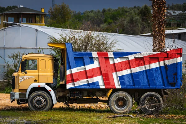 Dump truck with the image of the national flag of Iceland is parked against the background of the countryside. The concept of export-import, transportation, national delivery of goods