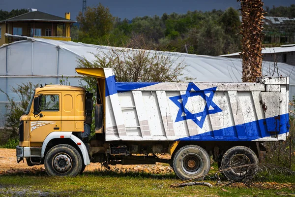 Dump truck with the image of the national flag of Israel is parked against the background of the countryside. The concept of export-import, transportation, national delivery of goods