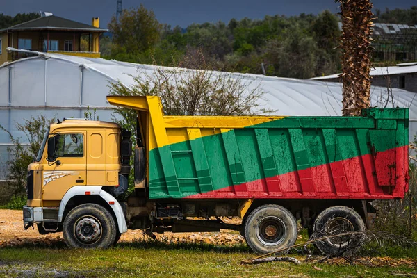 Dump truck with the image of the national flag of Lithuania is parked against the background of the countryside. The concept of export-import, transportation, national delivery of goods