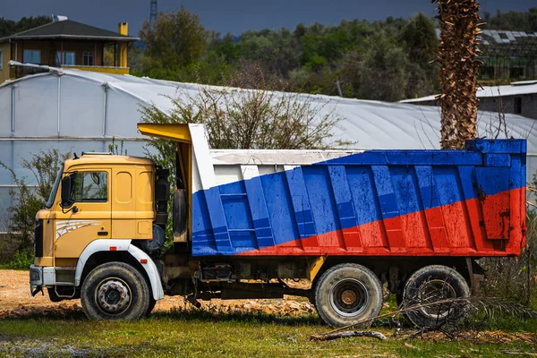 Dump truck with the image of the national flag of Russia is parked against the background of the countryside. The concept of export-import, transportation, national delivery of goods