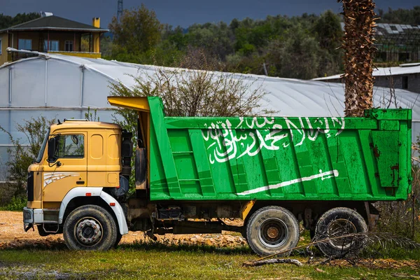 Dump truck with the image of the national flag of Saudi Arabia is parked against the background of the countryside. The concept of export-import, transportation, national delivery of goods