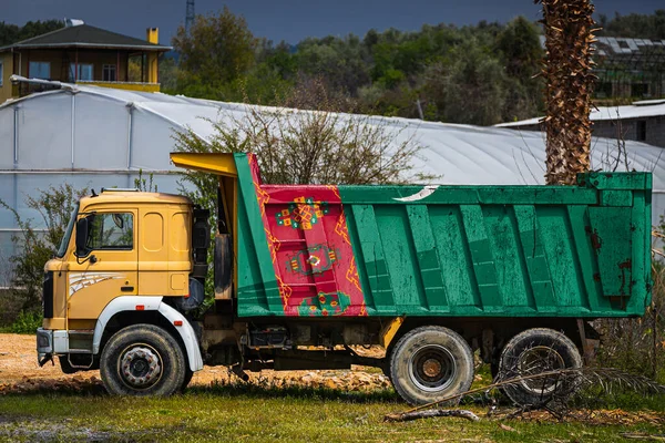 Dump truck with the image of the national flag of Turkmenistan is parked against the background of the countryside. The concept of export-import, transportation, national delivery of goods