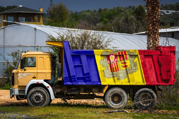 Dump truck with the image of the national flag of Andorra is parked against the background of the countryside. The concept of export-import, transportation, national delivery of goods