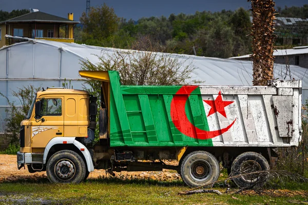 Dump truck with the image of the national flag of Algeria is parked against the background of the countryside. The concept of export-import, transportation, national delivery of goods