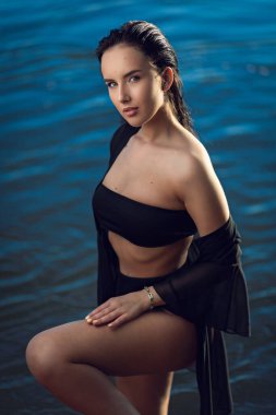 Siyah mayo ve açık renk pelerinli güzel bir esmer kadın deniz kıyısında dinleniyor. Tropik deniz sahilinde güzel, sıska bir kız.