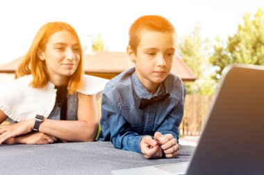 Anne çocuğuna evde bahçede ders veriyor, evde eğitim veriyor. Anne oğlunun ödevine yardım ediyor. Stres yapıyor. Bilgisayarla çevrimiçi okul dersleri