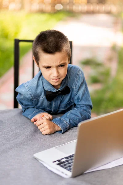 陽気な少年は庭の自宅でノートパソコンを通してレッスンに従事しています 子供のためのオンラインクラス — ストック写真