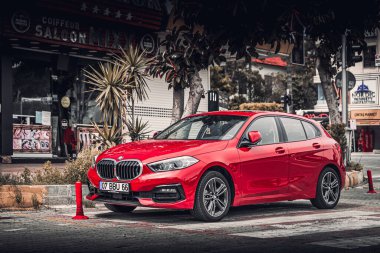 Alanya, Türkiye 17 Nisan 2021: Kırmızı BMW 1 serisi bir binanın arka planına, dükkanlara karşı kentteki caddeye park edildi 