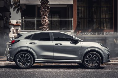 Alanya, Türkiye 12 Nisan 2021: Gümüş rengi Ford Puma bir binanın, dükkanların, ağaçların önüne park edilmiş. 