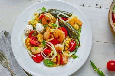 Beyaz bir tabakta servis edilen kabaklı makarna, karides, mini mozzarella, mısır ve ızgara sebzeli sağlıklı Akdeniz yemeği. Üst görünüm, düz görünüm.