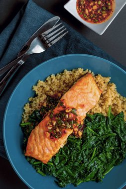 Izgara somon, kinoa ve ıspanak içeren temiz yemek tabağı, otlarla süslenmiş ve lezzetli bir sosla servis edilmiş, sağlıklı beslenme ve lezzete vurgu ile fotoğraflanmış. Düz Yatay Fotoğrafçılık.