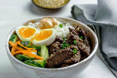 Taze et, kabarık beyaz pirinç, renkli havuç şeritleri, salatalık sarısı ve susam tohumlarıyla süslenmiş zengin yumurta sarısı karışımı bir Çin yemeği kasesi..