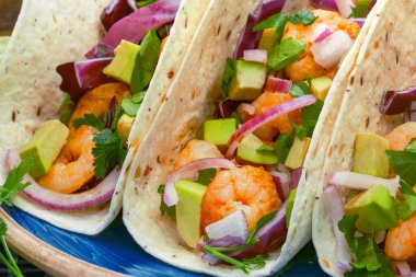 Renkli sebzeli garnitür ve limon dilimli taze karides tortilla paketleri, günlük yemek görüntüsü için damalı bir bez üzerinde mavi bir tabakta sunulur..