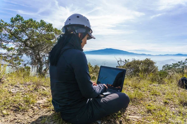 A portrait of a freelancer woman with a laptop sitting on a rock in a top mountain