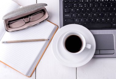 Bilgisayar, defter, bir fincan kahve ve bir kalem.