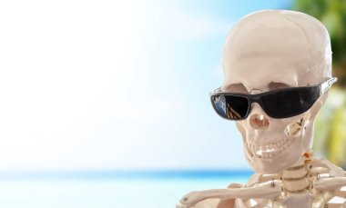 Tropik bir plajda gözlüklü insan iskeleti.
