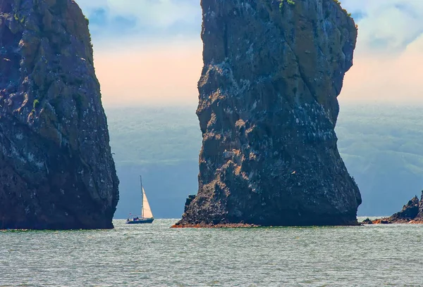 Sailboat sails near the coast and rocks on Kamchatka Peninsula