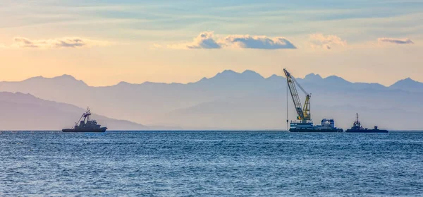 sea ship with a crane on the background of a mountain range in the haze