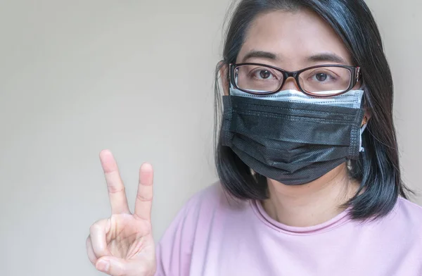 İki tıbbi maske takan Asyalı kadın portresi, iki parmak gösteriyor, Covid 19 Delta varyant virüsünü güçlü bir şekilde koruyacak kavram. Beyaz duvar arkaplanı ile ayarlanmış karıştırma resmi.
