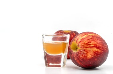 Annesiyle birlikte küçük bardakta organik elma sirkesi, camın yanında iki kırmızı elma, beyaz arkaplanda da görüntü var..