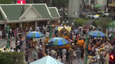 Erawan Tapınağı 'nın yoğun bir gündüz plazası yukarıdan ele geçirildi. Süslü altın tapınak, kalabalık bir kalabalık tarafından çevrelenmiş, saz çiçekleri ve çiçeklerle çevrili..