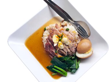 Tayland usulü ağır ateşte pişmiş domuz eti ve pirinç tabağının tepesi: dilimlenmiş, taze domuz pirincin üzerinde, üzerinde dilimlenmiş sarımsak ve doğranmış biber, yanında da salamura yeşillikler ve lezzetli bir kahverengi sosta pişirilmiş yarım yumurta; bir çatal ve bir çatal bulunur.