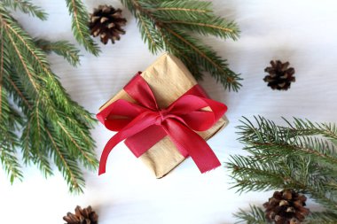 Masanın üstünde kırmızı bir fiyonk, üzerinde köknar dalları ve koniler olan el sanatları kağıdıyla kaplı bir kutu. Noel için Noel hediyesi