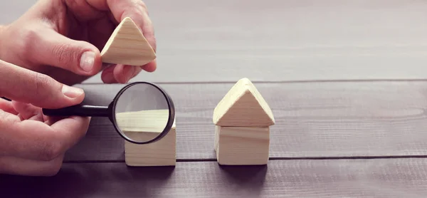 one hand lifts the roof of the house and the other holds a magnifying glass. close inspection of the property