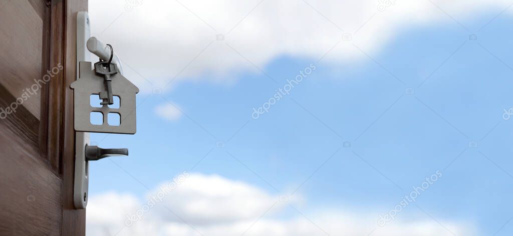 key with a house keychain hanging on the door handle, against a blue sky with clouds. offer of individual real estate
