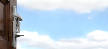 Bir evden anahtarlık ve açık ahşap bir kapının sapında asılı bir anahtar bulutlu mavi bir gökyüzüne karşı. ülke mülkiyeti