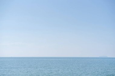 Denizin üzerinde güneş ışığıyla güzel bir gökyüzü. Su yüzeyinin sakin deniz uyumu. Güneşli gökyüzü ve mavi okyanus. Ufukta bulutlar olan canlı bir deniz.