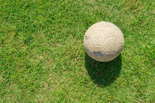 Old soccer ball on green grass of soccer field. Vintage football.