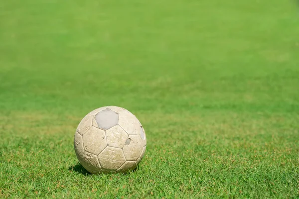 Old soccer ball on green grass of soccer field. Vintage football.